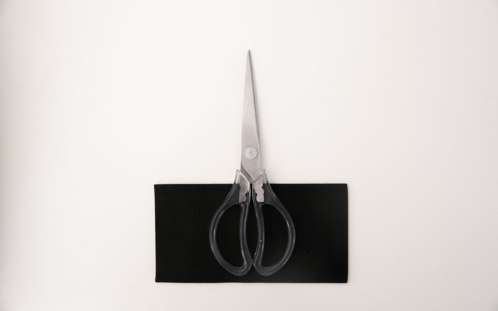 Pair of scissors with black handles resting on a piece of black fabric