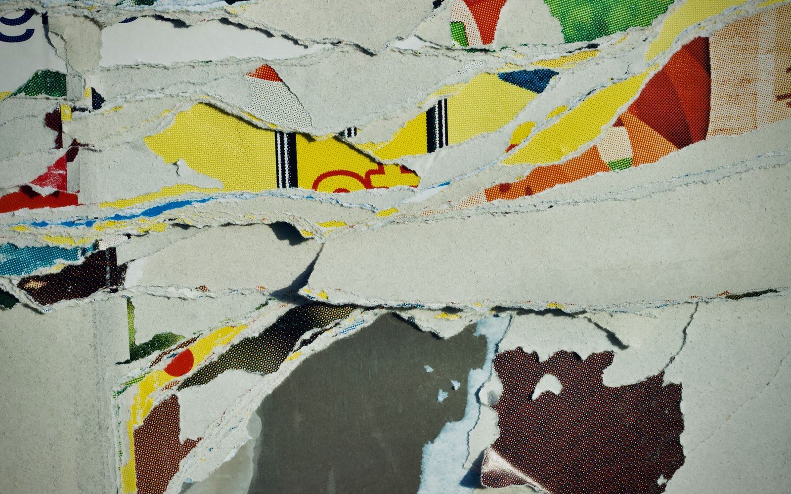 Layers of torn colorful posters reveal fragments of underlying advertisements beneath cracked plaster