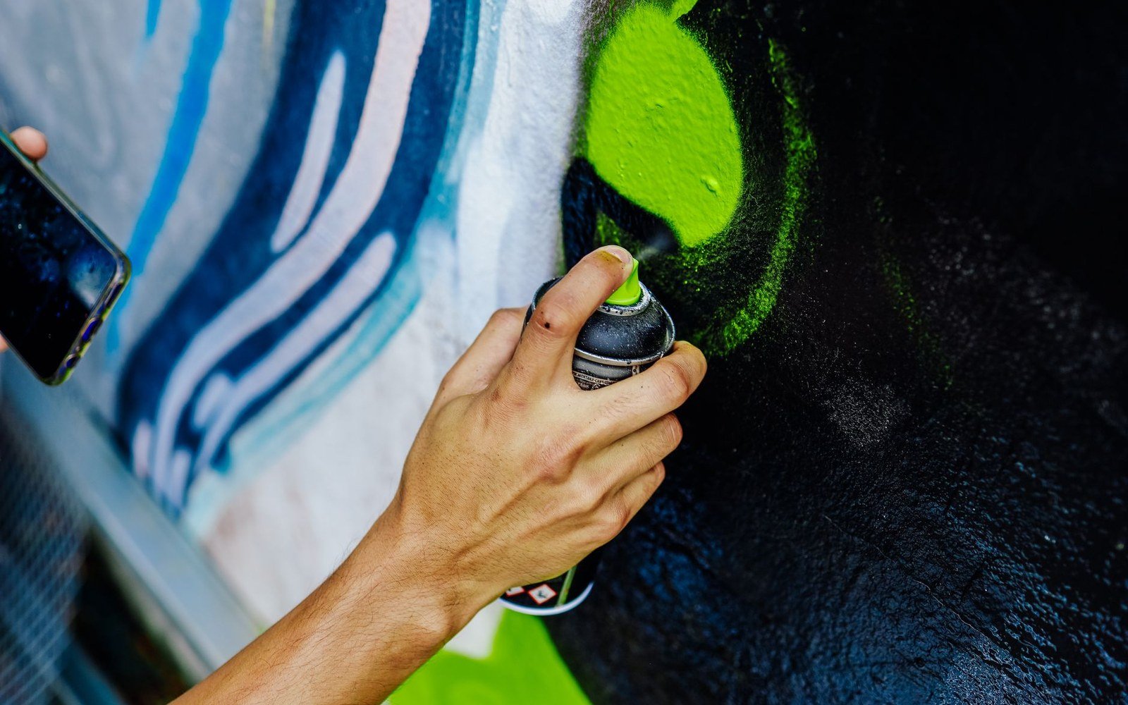 A hand sprays green paint from an aerosol can onto a mural