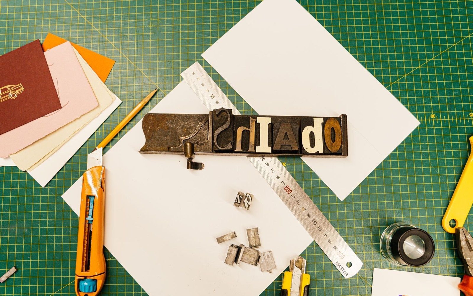 Wooden letterpress type blocks locked in a composing stick alongside rulers and craft knives