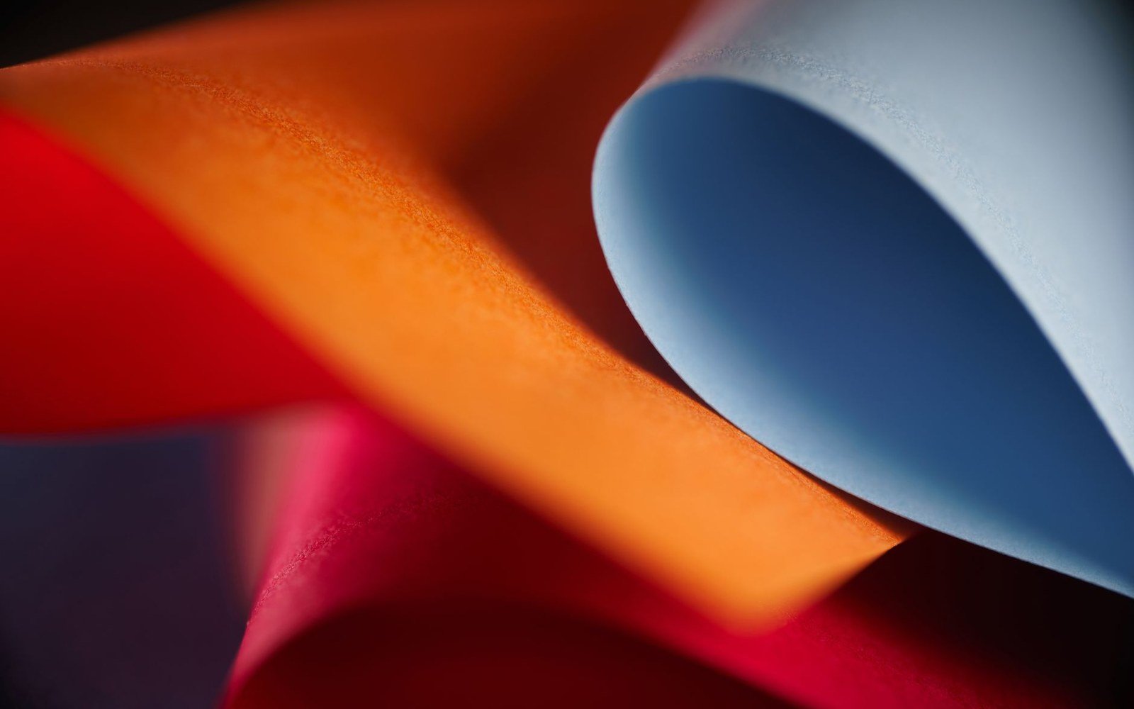 Curled sheets of orange, red and pale blue paper form looping folds