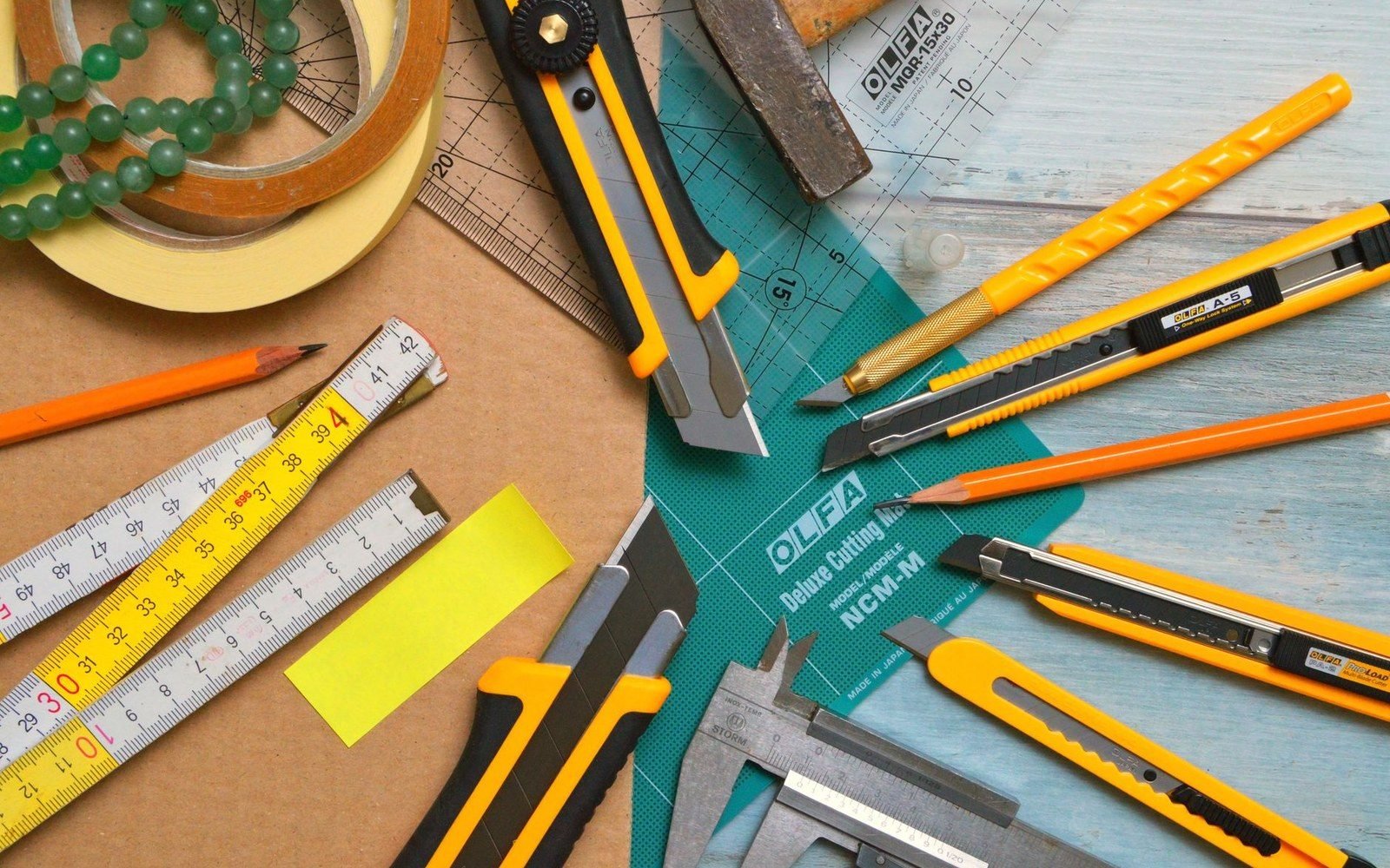 A scalpel and a steel rule lying parallel on a cutting mat, both marked with use